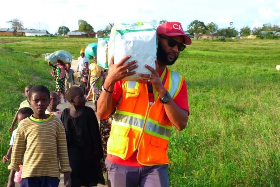 A Helping Hands volunteer carrying a food sack on his shoulder, walking with children and families from the village